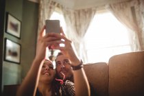 Heureux couple prendre selfie tandis que assis sur canapé à la maison — Photo de stock