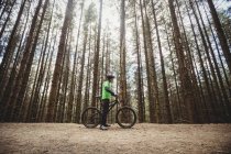 Vista lateral do ciclista de montanha na estrada de terra contra árvores na floresta — Fotografia de Stock