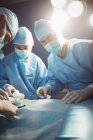 Хирург смотрит в камеру, пока коллеги выполняют операцию в операционной — стоковое фото