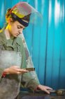 Soldador fêmea examinando peça de metal na oficina — Fotografia de Stock