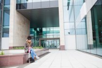 Молода жінка з цифровий планшетний сидячи за межами Офісна будівля — стокове фото