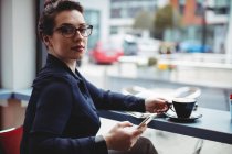 Retrato de mujer de negocios sosteniendo el teléfono móvil en la cafetería - foto de stock