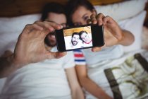 Couple prenant selfie photo de téléphone mobile sur le lit dans la chambre — Photo de stock