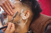 Uomo ottenere la barba rasata con rasoio in negozio di barbiere — Foto stock