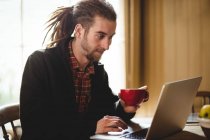 Jeune homme hipster utilisant un ordinateur portable à la maison — Photo de stock
