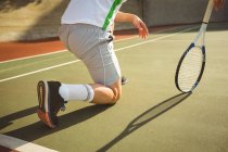Homem ajoelhado na corte enquanto joga tênis à luz do sol — Fotografia de Stock