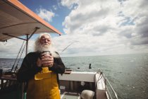 Вдумливий рибалка стоїть на човні з чашкою кави — стокове фото
