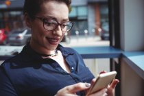 Усміхнена молода жінка використовує мобільний телефон у кафе — стокове фото