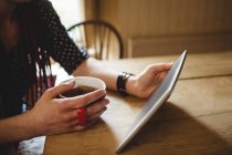 Midsection de mulher usando tablet enquanto toma café em casa — Fotografia de Stock