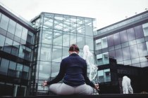 Вид ззаду бізнес-леді робить йогу проти офісної будівлі — стокове фото