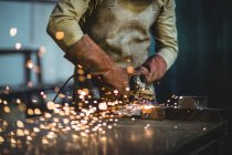 Abgeschnittenes Bild eines Schweißers, der in der Werkstatt an einem Metallstück arbeitet — Stockfoto