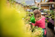Female florist watering plant with watering can in garden centre — Stock Photo