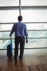 Vue arrière d'un homme d'affaires avec des bagages regardant par une fenêtre vitrée à l'aéroport — Photo de stock