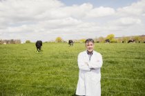 Portrait of confident vet standing on grassy field against cloudy sky — Stock Photo