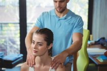 Fisioterapeuta masajeando hombro de paciente femenina en clínica - foto de stock