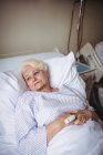 Задумчивая пожилая женщина на кровати в больнице — стоковое фото