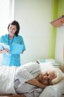 Paciente mayor durmiendo en una cama mientras la enfermera revisa el informe en el hospital - foto de stock
