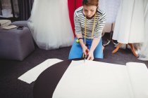 Female fashion designer cutting white fabric in studio — Stock Photo