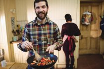 Мужчина готовит еду на кухне дома с женщиной на заднем плане — стоковое фото