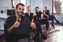 Portrait of smiling hairdressers showing thumbs up in salon — Stock Photo
