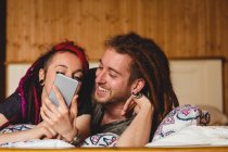 Jovem casal hipster usando telefone celular na cama em casa — Fotografia de Stock
