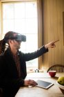Hipster pointing while wearing virtual reality simulator at home — Stock Photo