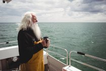 Thoughtful fisherman standing on boat with cup of coffee — Stock Photo
