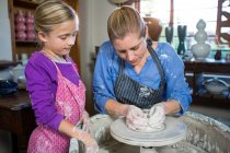 Alfarero femenino ayudando a chica en taller de cerámica - foto de stock