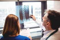 Rückansicht Arzt untersucht Röntgenbild, während Krankenschwester im Krankenhaus auf Klemmbrett schreibt — Stockfoto