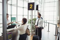 Mujer dando su pasaporte a la azafata de check-in de la aerolínea en el mostrador de check-in del aeropuerto - foto de stock