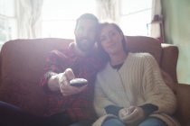 Paar sitzt auf Sofa mit Fernbedienung, während es im heimischen Wohnzimmer fernsieht — Stockfoto
