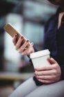 Midsection of businesswoman holding cellphone and disposable coffee cup — Stock Photo