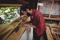 Homem que mede uma prancha de madeira no estaleiro — Fotografia de Stock