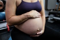 Partie médiane de la femme enceinte assise sur le ballon d'exercice dans la salle de gym — Photo de stock