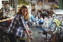 Portrait of beautiful mechanic trying bicycle in workshop — Stock Photo