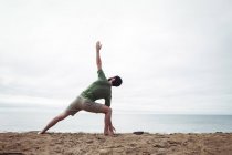 Vista trasera del hombre realizando ejercicio de estiramiento en la playa - foto de stock