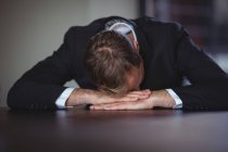 Empresário exausto sentado de cabeça para baixo na mesa do escritório — Fotografia de Stock