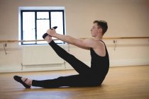Seitenansicht des Ballerinos, der sich auf dem Holzboden im Ballettstudio dehnt — Stockfoto