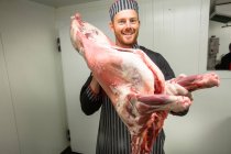 Мясник держит свиную тушу в мясной лавке — стоковое фото
