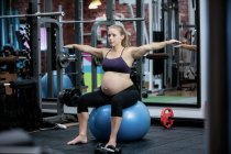 Femme enceinte préformant exercice d'étirement sur balle de fitness dans la salle de gym — Photo de stock