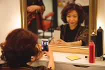 Donna elegante che prende selfie di specchio a salone di capelli — Foto stock