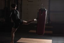 Visão traseira do Boxer masculino praticando boxe com saco de perfuração no estúdio de fitness — Fotografia de Stock