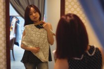 Frau schaut in Spiegel, während sie in Boutique-Geschäft ein Oberteil probiert — Stockfoto