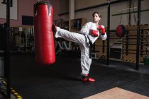 Handsome Man practicing karate with punching bag in fitness studio — Stock Photo