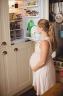 Mulher grávida à procura de alimentos na geladeira na cozinha — Fotografia de Stock