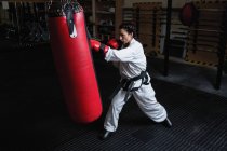 Jeune femme pratiquant le karaté avec sac de boxe dans un studio de fitness — Photo de stock