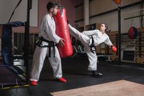 Man and woman practicing karate with punching bag in studio — Stock Photo