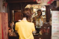 Donna che indossa una collana vintage e si guarda allo specchio nel negozio di antiquariato — Foto stock