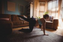 Беременная женщина, выполняющая упражнения на растяжку в гостиной дома — стоковое фото
