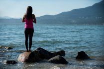 Вид ззаду жінки, що виконує йогу на скелі на пляжі — стокове фото